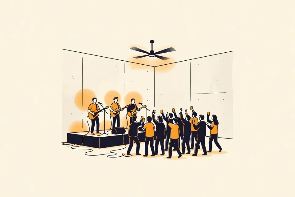 A wide shot of a concrete live music venue with a low stage, three bands performing, and a small audience holding up phones. A ceiling fan spins above the hazy air.